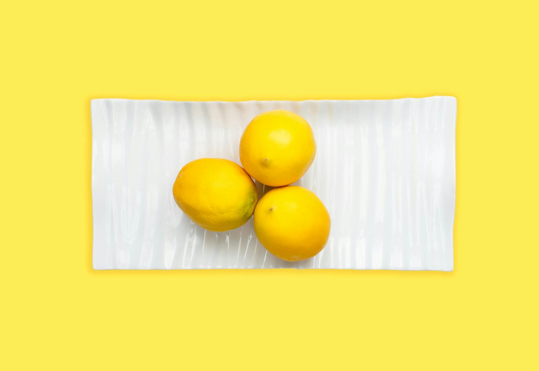 Hand holding a fresh lemon against a bright yellow background, symbolizing the refreshing sensation of a lemon vibrator.