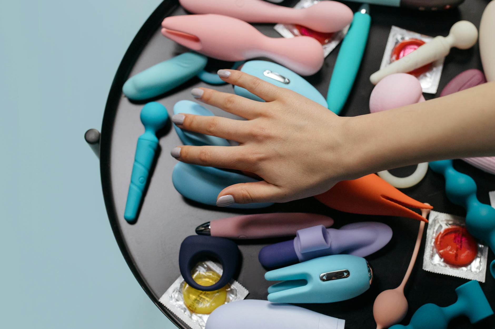 Hand reaching over a variety of colorful lemon vibrators and adult toys arranged on a table.
