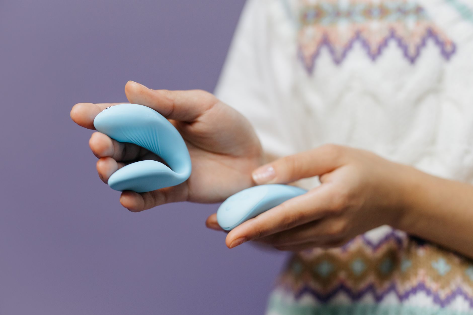 Close-up of hands holding a sleek blue vibrator against a purple background, emphasizing intimate relaxation.