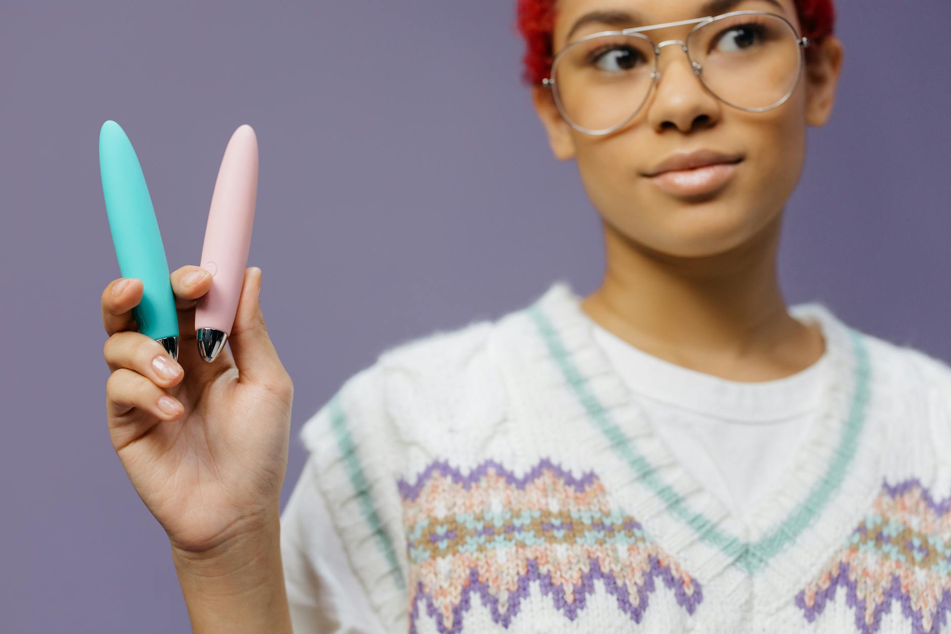 A woman holding colorful vibrators against a purple background, exploring pleasure options