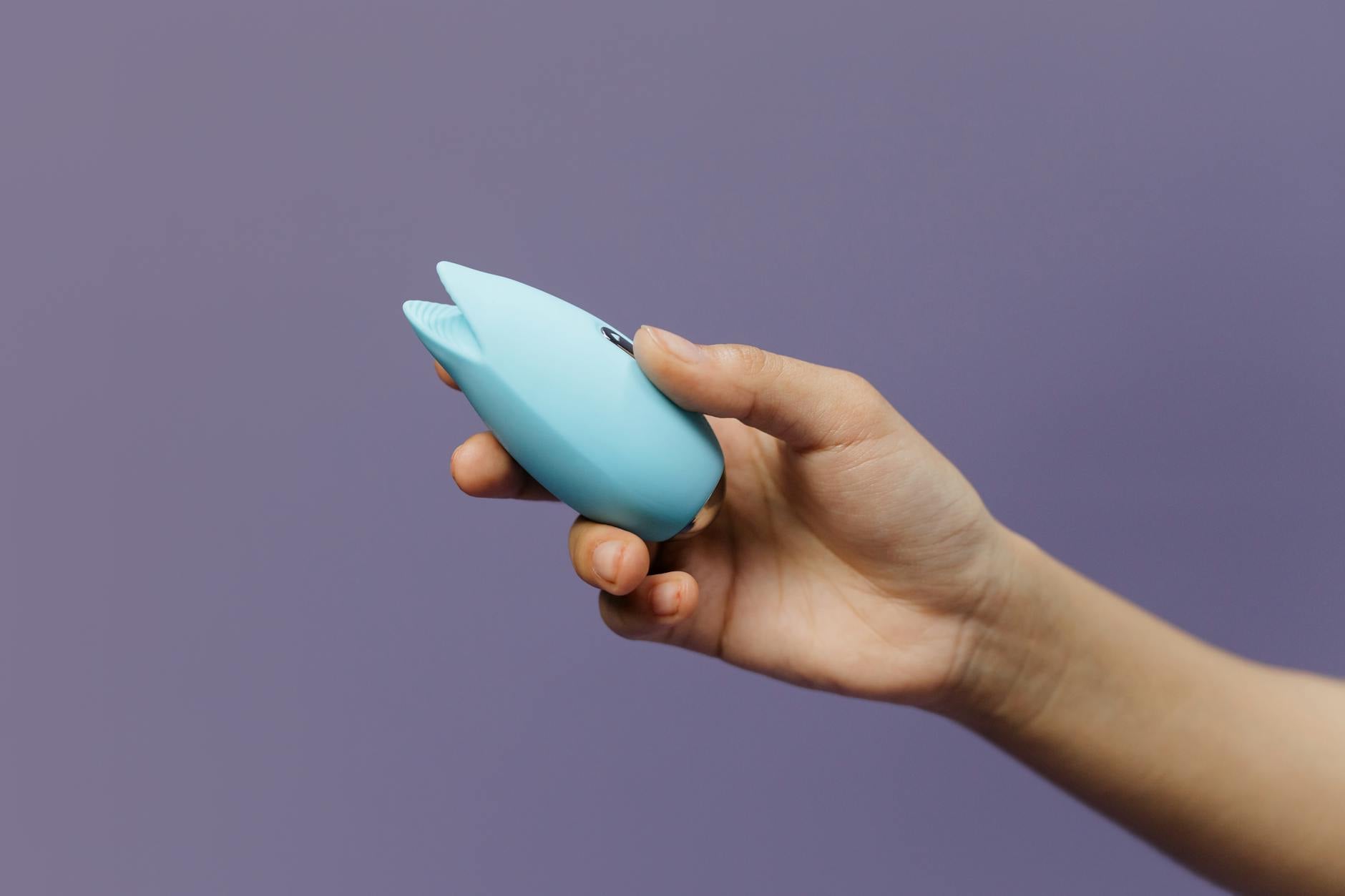 A blue silicone vibrator held against a solid purple background, symbolizing self-paced pleasure and personal choice