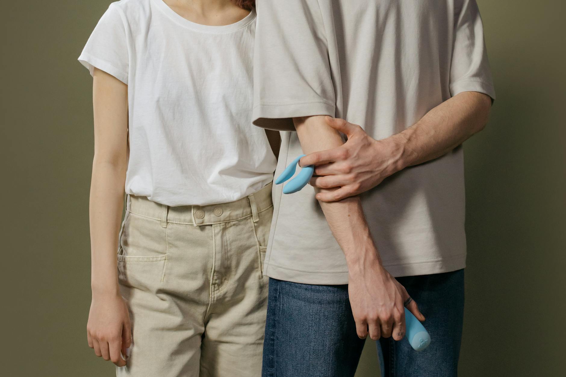 A couple standing together indoors, holding a blue vibrator, symbolizing modern intimacy and reconnection.